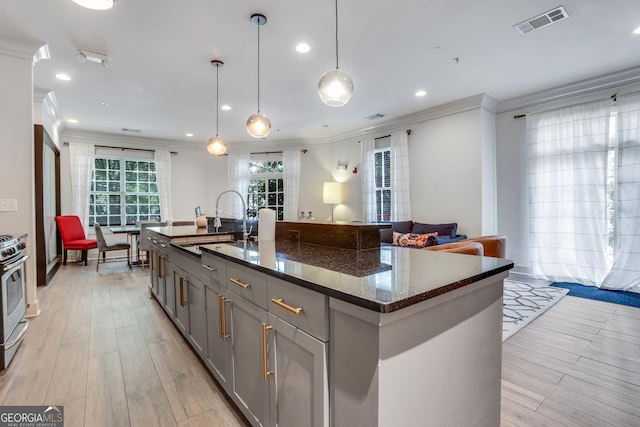 kitchen with gray cabinets, ornamental molding, a sink, dark stone countertops, and light wood-style floors