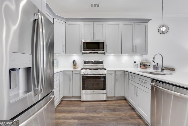 kitchen with appliances with stainless steel finishes, a sink, light countertops, ornamental molding, and gray cabinets