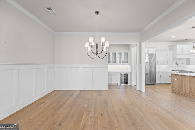 2824 Cork St, Braselton, GA 30517 - unfurnished dining area featuring wine cooler, ornamental molding, light wood-style flooring, a chandelier, and a wainscoted wall
