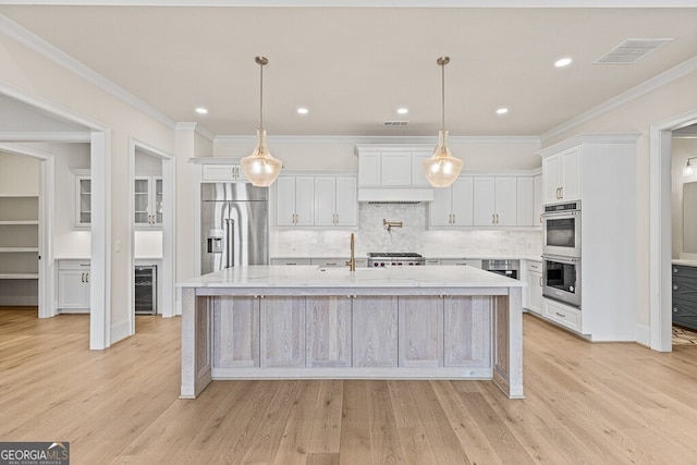 2824 Cork St, Braselton, GA 30517 - kitchen with stainless steel appliances, wine cooler, light wood-style floors, a large island with sink, and crown molding