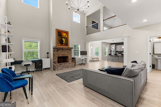living room with light wood-type flooring, a high ceiling, a chandelier, and a fireplace