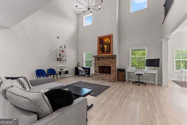 living area featuring a high ceiling, a brick fireplace, a chandelier, baseboards, and wood finished floors