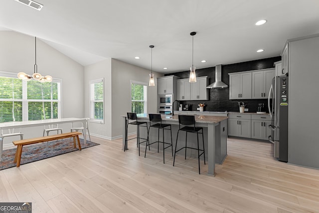 kitchen featuring wall chimney range hood, a breakfast bar area, stainless steel appliances, backsplash, and visible vents