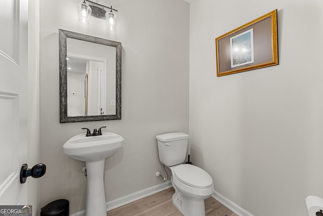 half bathroom with baseboards, a sink, wood finished floors, and toilet
