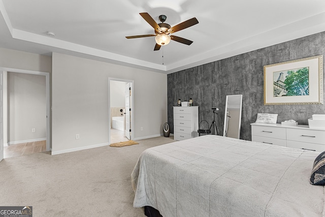 bedroom featuring a ceiling fan, a raised ceiling, baseboards, ensuite bathroom, and light carpet