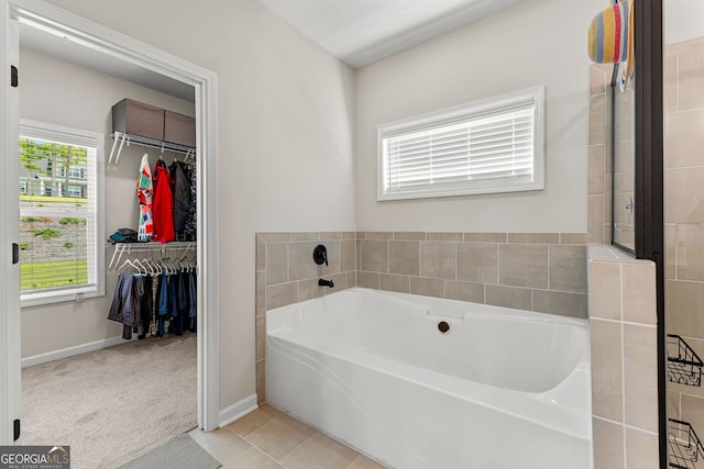 bathroom with a walk in closet, baseboards, tile patterned flooring, and a bath