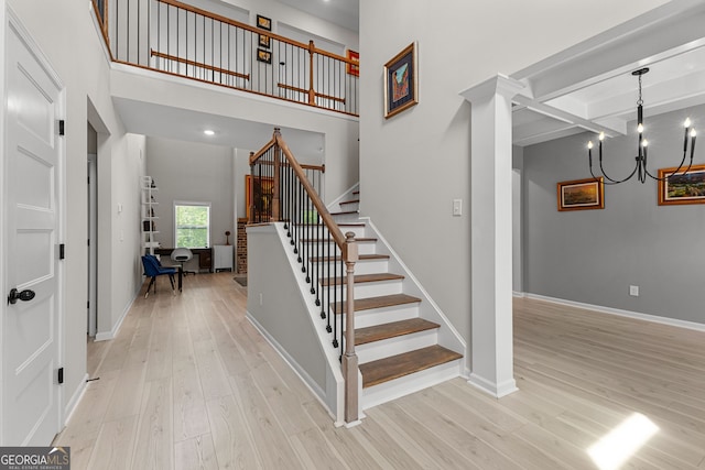 stairs featuring an inviting chandelier, baseboards, wood finished floors, a towering ceiling, and beamed ceiling