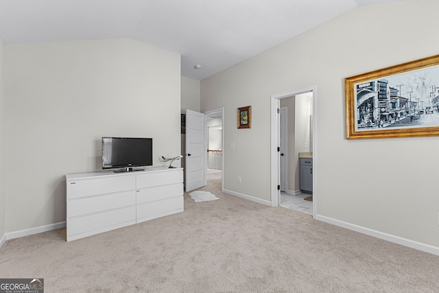 bedroom featuring light colored carpet, baseboards, vaulted ceiling, and ensuite bathroom