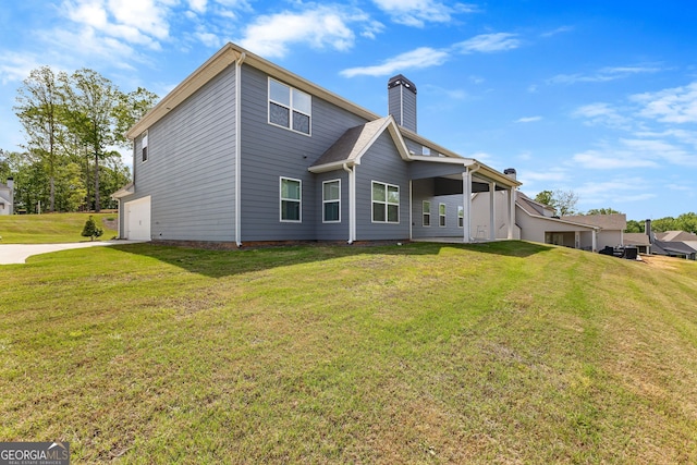 back of house featuring a garage, a yard, driveway, and a chimney