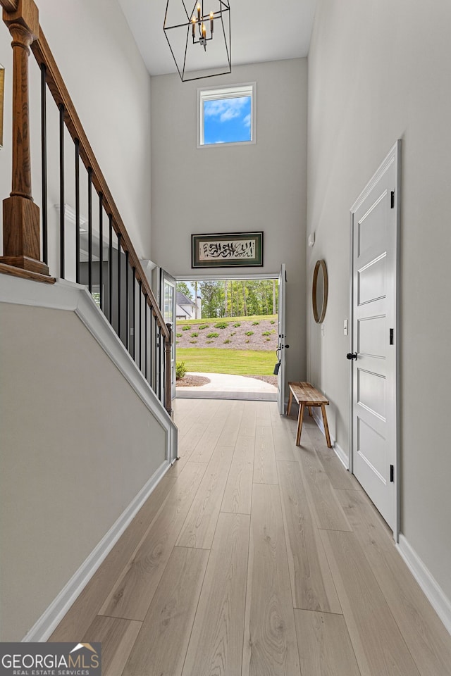 foyer featuring a towering ceiling, plenty of natural light, wood finished floors, and a chandelier