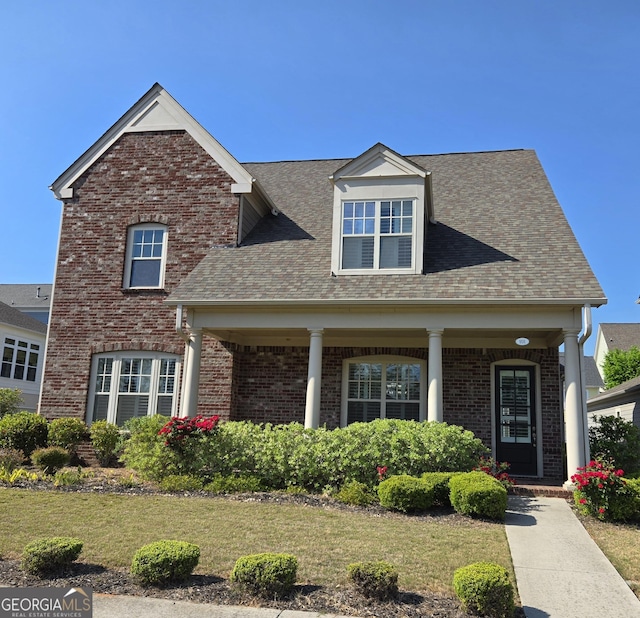 view of front of home with brick siding, a front lawn, roof with shingles, and a porch