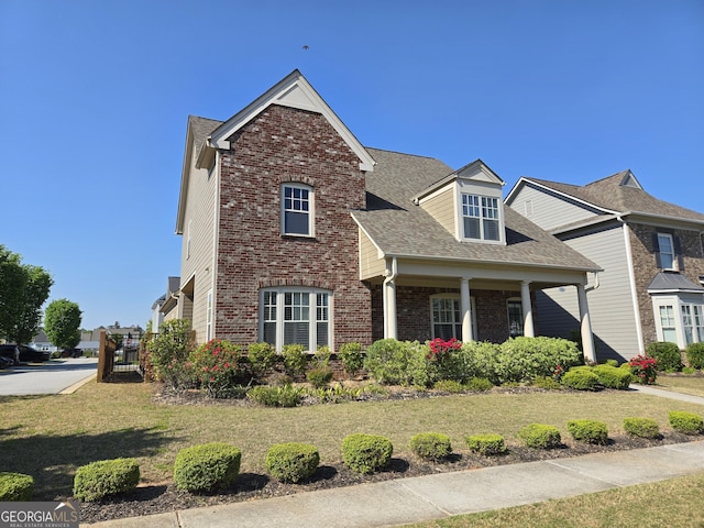 view of front of house featuring roof with shingles, a front yard, and brick siding