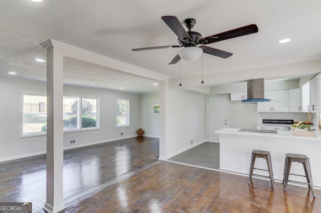 kitchen featuring wall chimney exhaust hood, a peninsula, open floor plan, white cabinetry, and visible vents