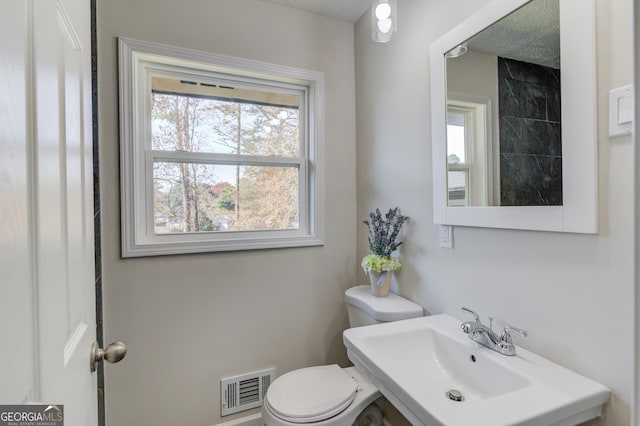 bathroom featuring toilet, a wealth of natural light, visible vents, and a sink