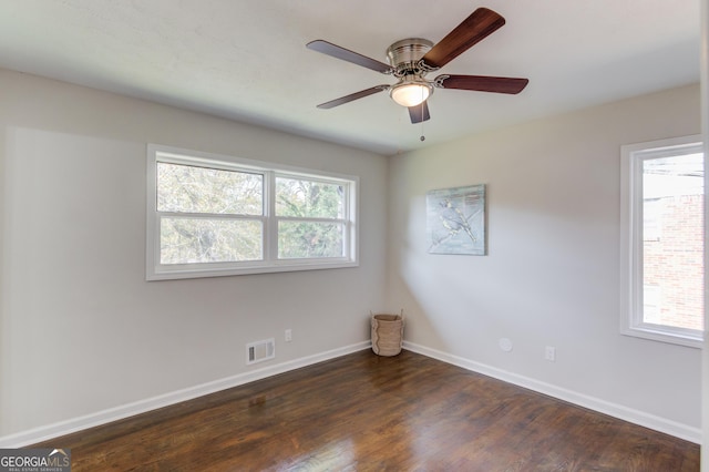 empty room featuring dark wood-style floors, baseboards, visible vents, and plenty of natural light