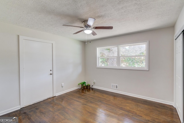 spare room with wood finished floors, a textured ceiling, visible vents, a ceiling fan, and baseboards