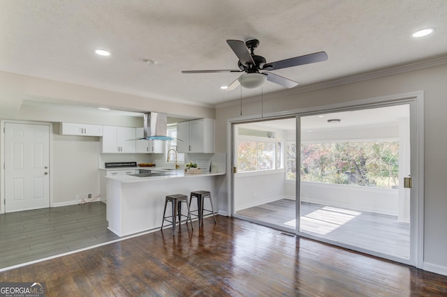 kitchen featuring a peninsula, baseboards, white cabinets, a sink, and exhaust hood