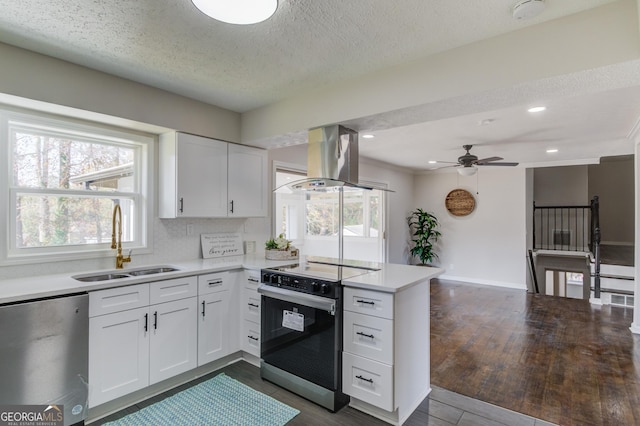 kitchen with a peninsula, dishwashing machine, island range hood, a sink, and range with electric cooktop