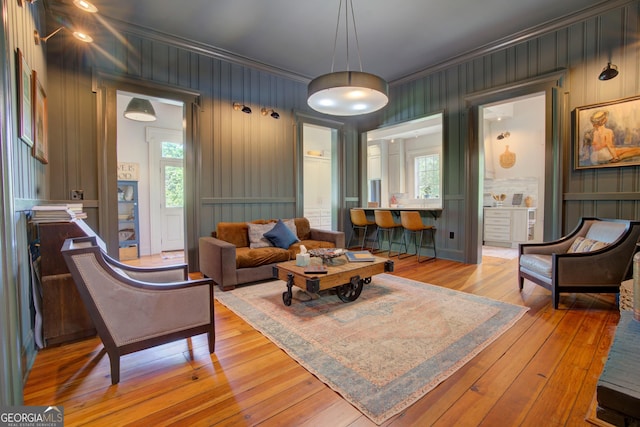 living room featuring crown molding, light wood-style floors, and a decorative wall