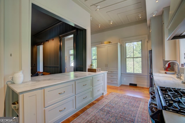 kitchen with light wood-style floors, ornamental molding, open shelves, and light stone counters