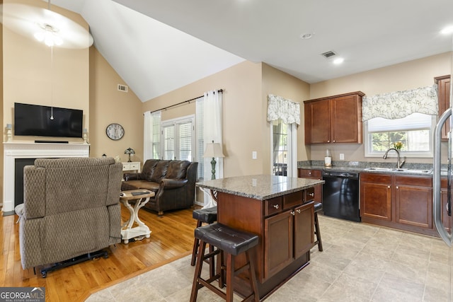 kitchen with visible vents, open floor plan, black dishwasher, a sink, and dark stone countertops