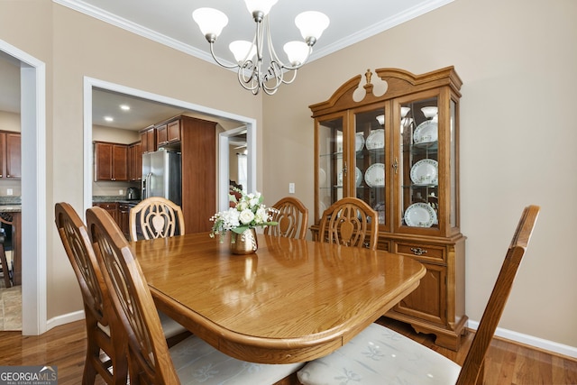 dining space with an inviting chandelier, baseboards, crown molding, and wood finished floors