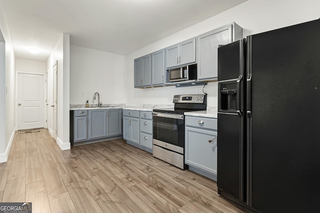 kitchen featuring appliances with stainless steel finishes, a sink, light wood finished floors, light countertops, and gray cabinets