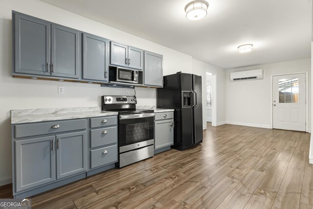 kitchen with gray cabinets, appliances with stainless steel finishes, a wall mounted AC, wood finished floors, and baseboards