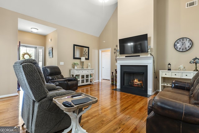 living area featuring visible vents, wood finished floors, baseboards, high vaulted ceiling, and a fireplace with flush hearth