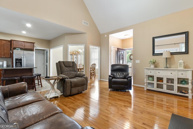 living room with visible vents, light wood-style floors, and high vaulted ceiling