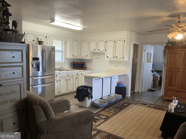kitchen featuring wood finished floors, ceiling fan, light countertops, white cabinets, and appliances with stainless steel finishes
