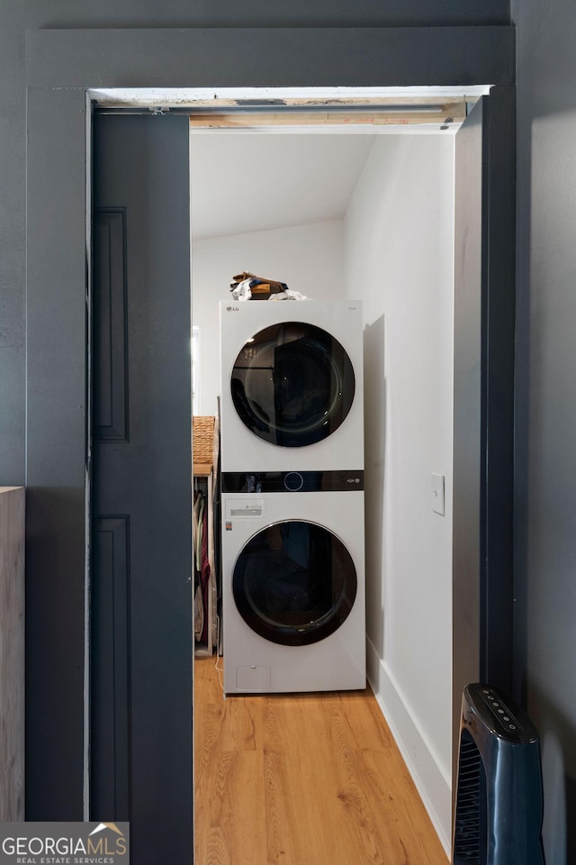 laundry area featuring stacked washer / dryer, light wood-type flooring, and baseboards
