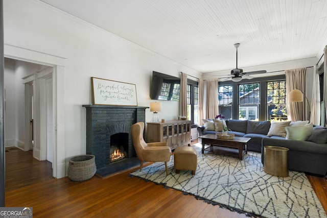 living room with wood finished floors, a brick fireplace, ceiling fan, and ornamental molding