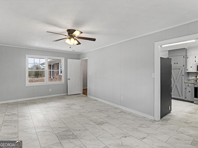 spare room featuring ceiling fan, wood walls, marble finish floor, baseboards, and ornamental molding