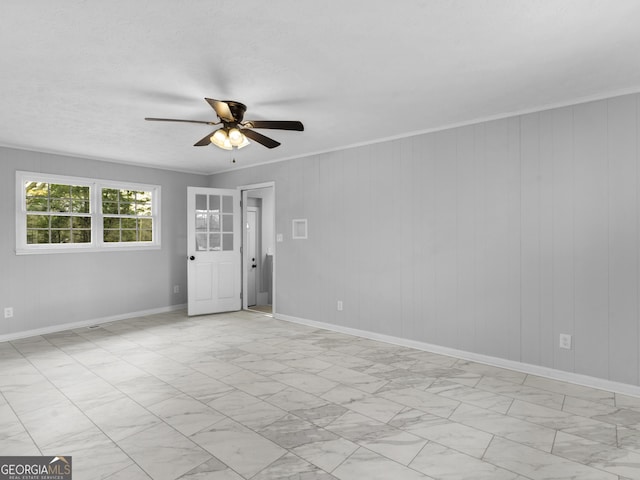 unfurnished room with crown molding, baseboards, a ceiling fan, and wood walls