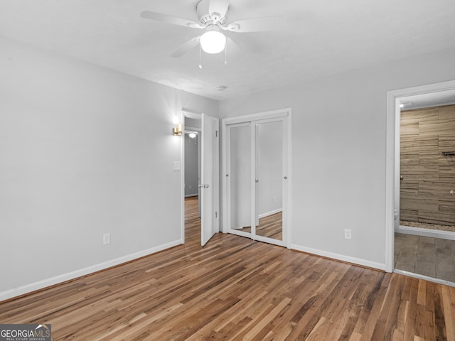 unfurnished bedroom featuring ceiling fan, wood finished floors, baseboards, a closet, and ensuite bath
