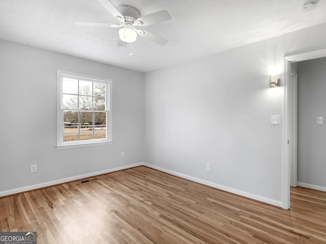 empty room with baseboards, a ceiling fan, wood finished floors, and visible vents