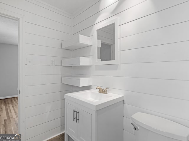 half bath with vanity, wood finished floors, toilet, baseboards, and wooden walls