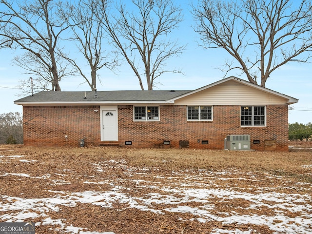 snow covered rear of property featuring brick siding, central AC, and crawl space