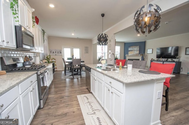 kitchen featuring an inviting chandelier, open floor plan, white cabinetry, a sink, and stainless steel appliances