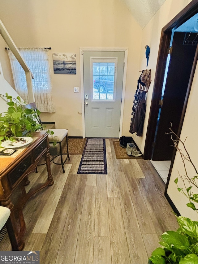 doorway with light wood-style floors and vaulted ceiling