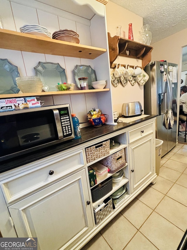 interior space with open shelves, appliances with stainless steel finishes, light tile patterned floors, and dark countertops