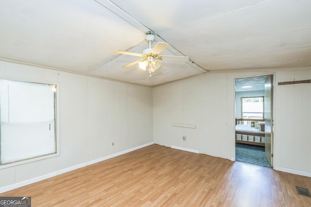 spare room featuring a ceiling fan, visible vents, baseboards, lofted ceiling, and light wood-style floors