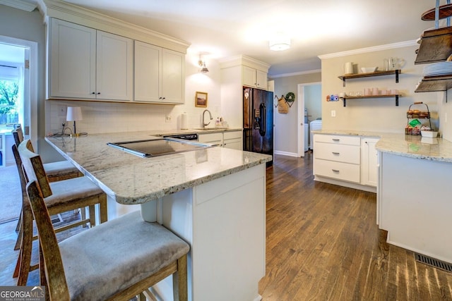 kitchen with open shelves, a peninsula, a sink, dark wood finished floors, and black appliances