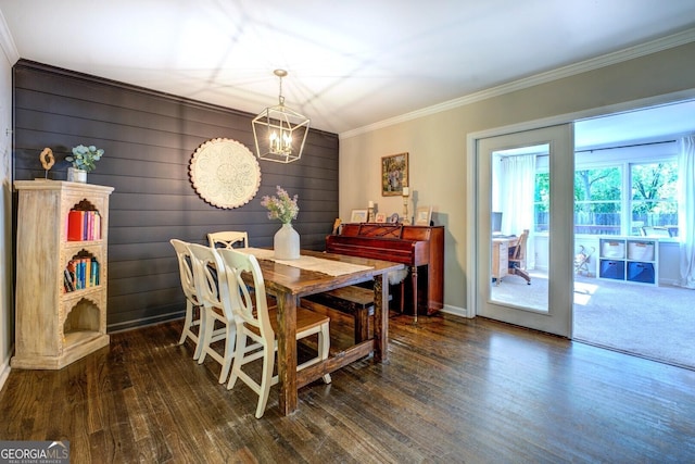 dining area with an inviting chandelier, wood walls, baseboards, wood finished floors, and ornamental molding