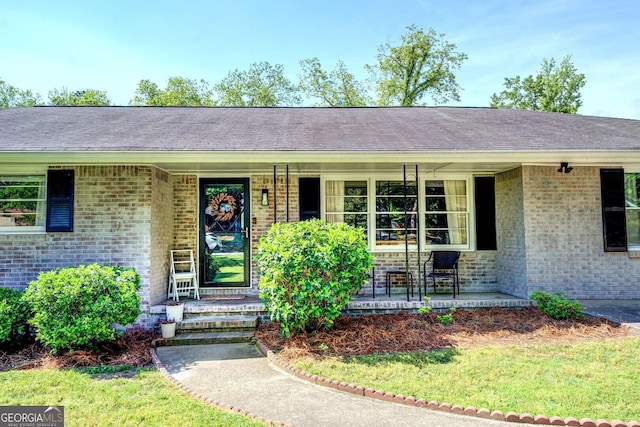 doorway to property featuring a porch and brick siding