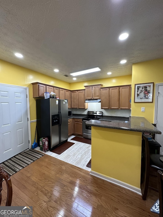 kitchen featuring dark wood-style flooring, ventilation hood, appliances with stainless steel finishes, and a breakfast bar area