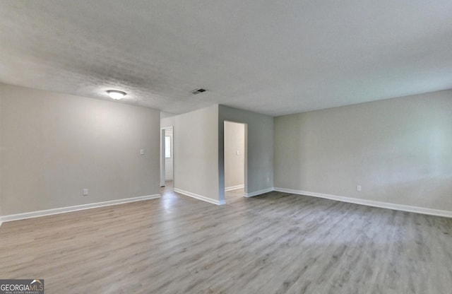 spare room featuring baseboards, visible vents, and wood finished floors