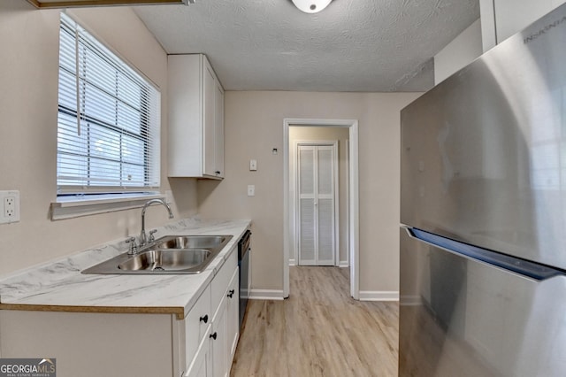 kitchen with a sink, white cabinets, freestanding refrigerator, light wood finished floors, and dishwashing machine