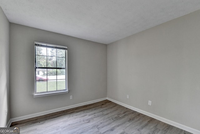 unfurnished room with a textured ceiling, baseboards, and wood finished floors